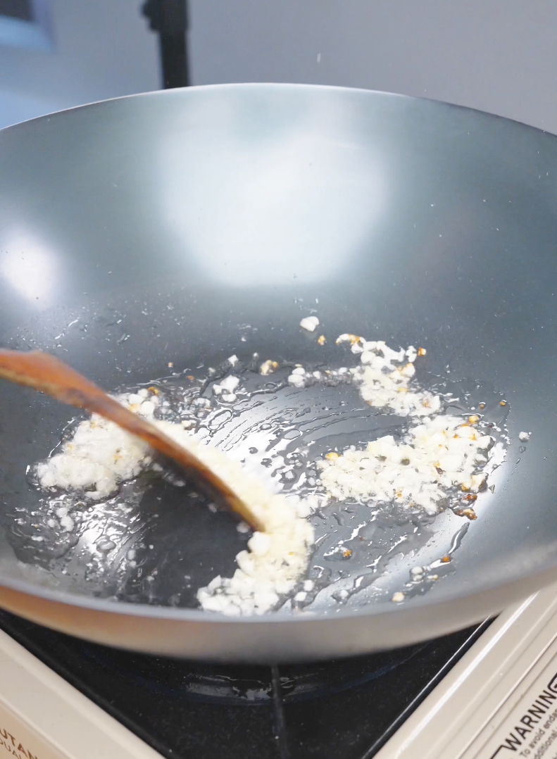 Minced garlic cooking in oil in a wok while starting Sticky Orange Chicken Recipe.