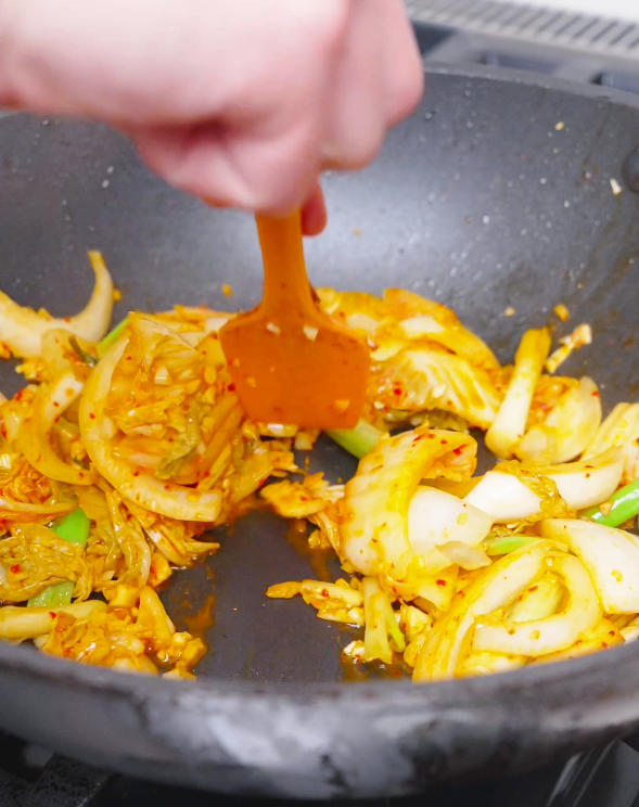 Kimchi and onions being stirred with a spatula in the pan for Kimchi Beef Stir Fry Recipe.