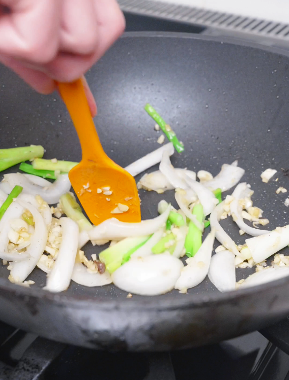 Sliced onions, scallions, and minced garlic being stirred in the pan for Teriyaki Beef Recipe.