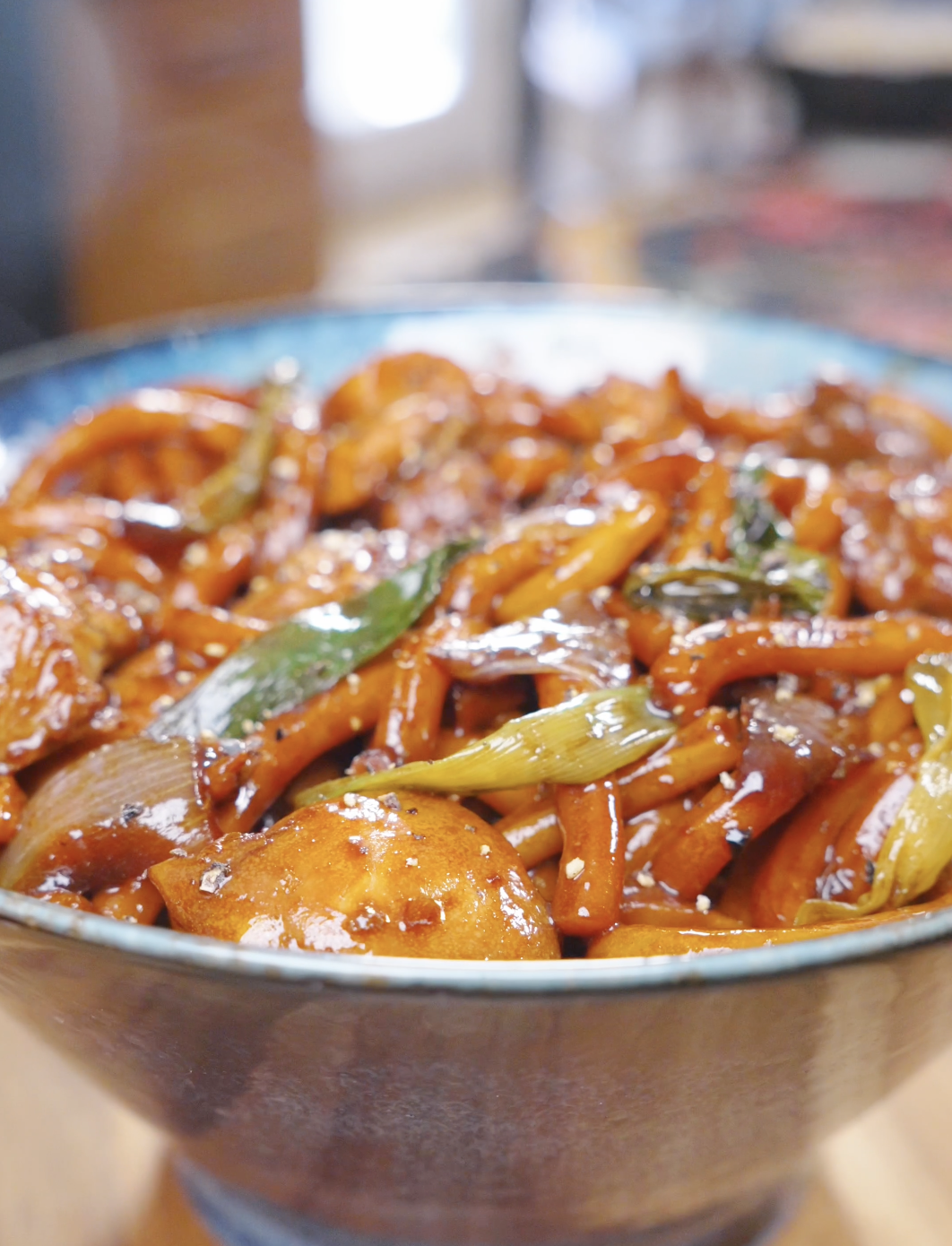 Finished Black Pepper Chicken Udon Recipe in a blue bowl with scallions and cracked black pepper.