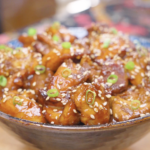 Finished Honey Sesame Chicken Recipe in a ceramic bowl topped with sesame seeds and sliced scallions.