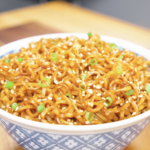 Finished Soy Butter Noodles Recipe in a blue patterned bowl topped with sesame seeds and scallions.