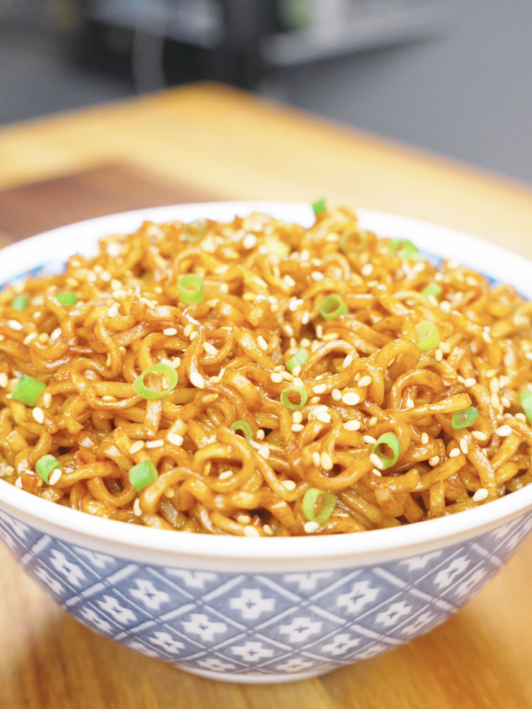 Finished Soy Butter Noodles Recipe in a blue patterned bowl topped with sesame seeds and scallions.