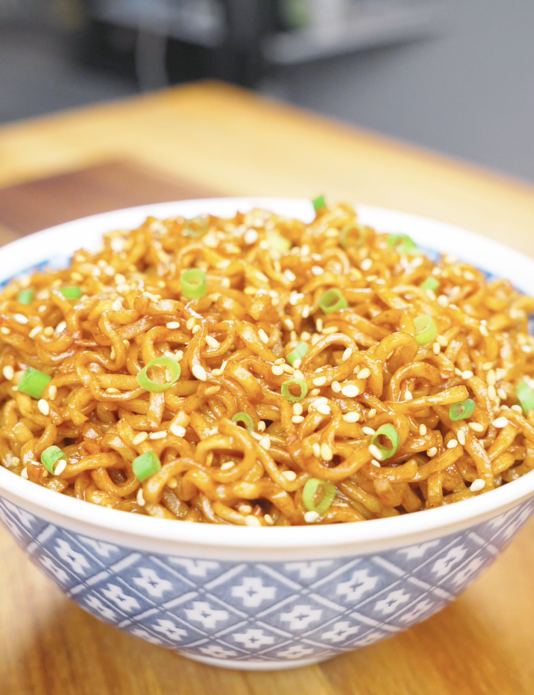Finished Soy Butter Noodles Recipe in a blue patterned bowl topped with sesame seeds and scallions.