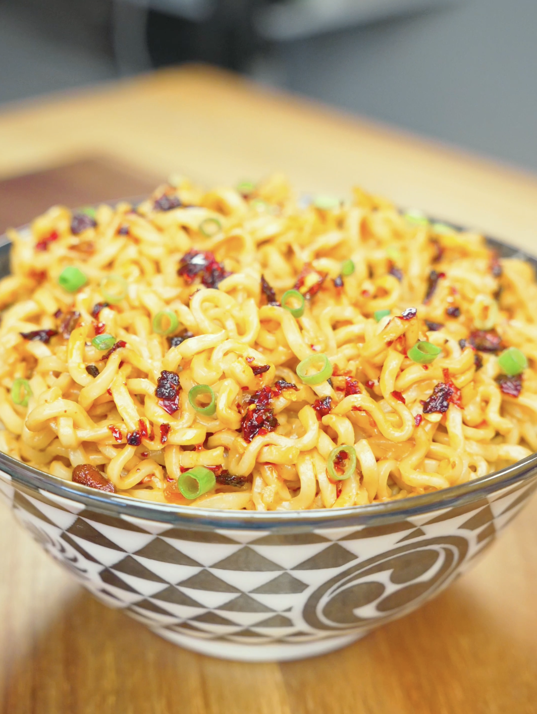 Finished Spicy Peanut Noodles Recipe in a patterned bowl topped with chili crisp and sliced scallions.