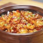 Finished Sticky Soy Garlic Chicken Recipe in a clay pot topped with sesame seeds and sliced scallions.