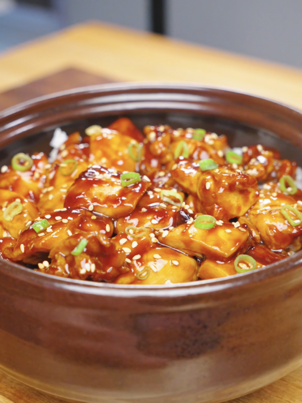 Finished Sticky Soy Garlic Chicken Recipe in a clay pot topped with sesame seeds and sliced scallions.