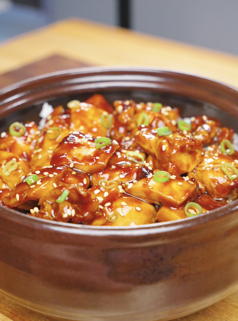 Finished Sticky Soy Garlic Chicken Recipe in a clay pot topped with sesame seeds and sliced scallions.