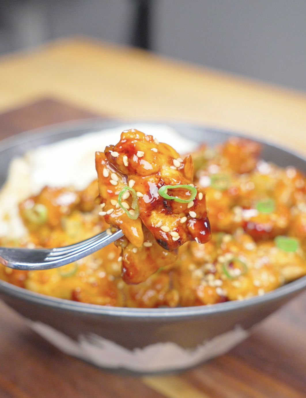 A fork lifting a glossy, sesame-coated piece above the bowl of Firecracker Chicken Recipe.
