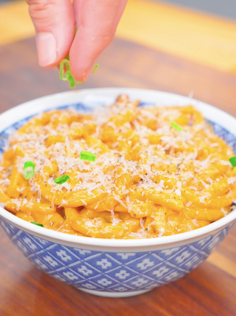 Sliced scallions being sprinkled over grated Parmesan on a bowl of Creamy Miso Butter Noodles Recipe.