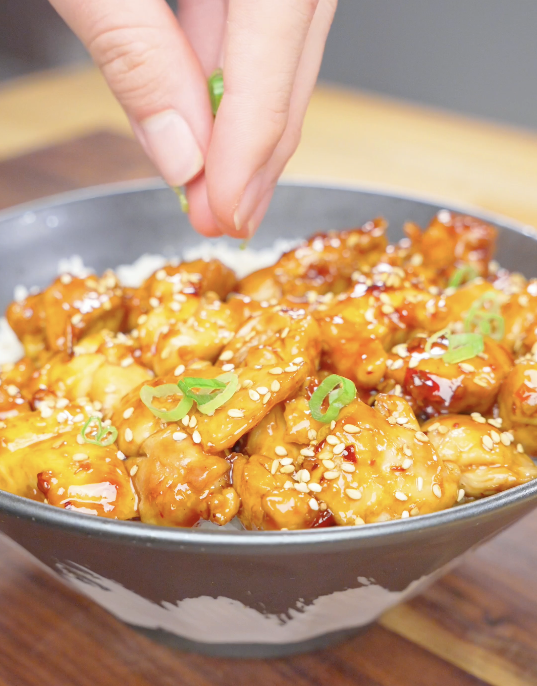 Sliced scallions being sprinkled over a sesame-topped rice bowl of Firecracker Chicken Recipe.