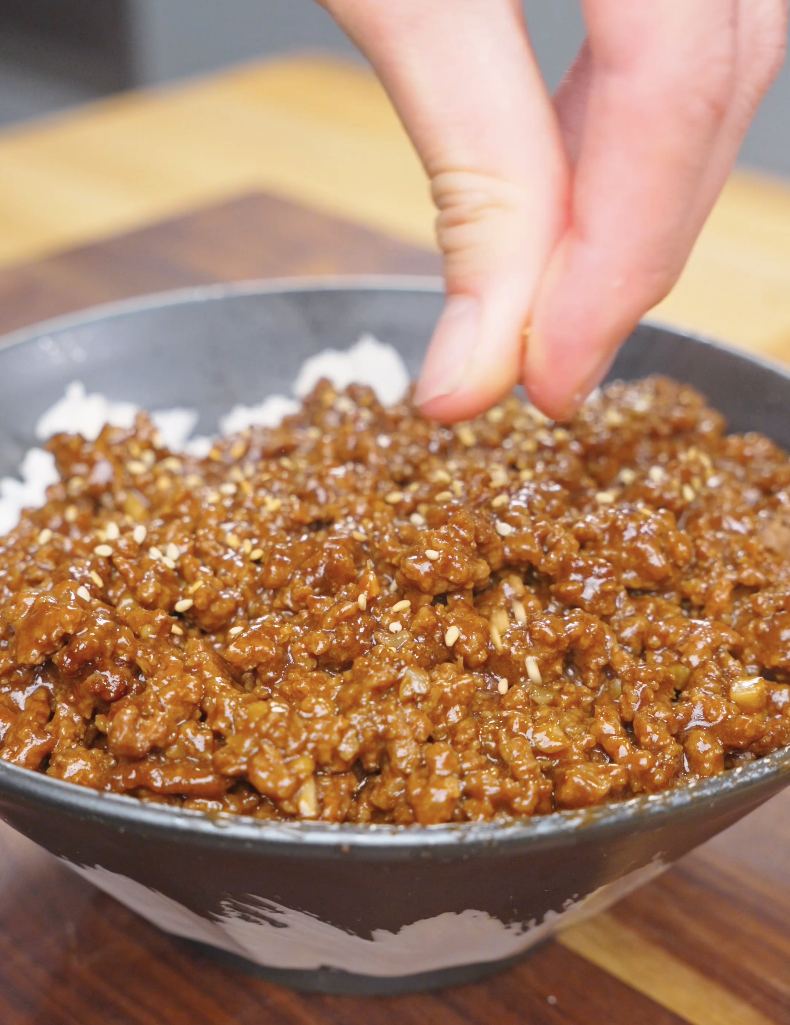 Sesame seeds being sprinkled over a rice bowl of Garlic Butter Ground Beef Recipe.