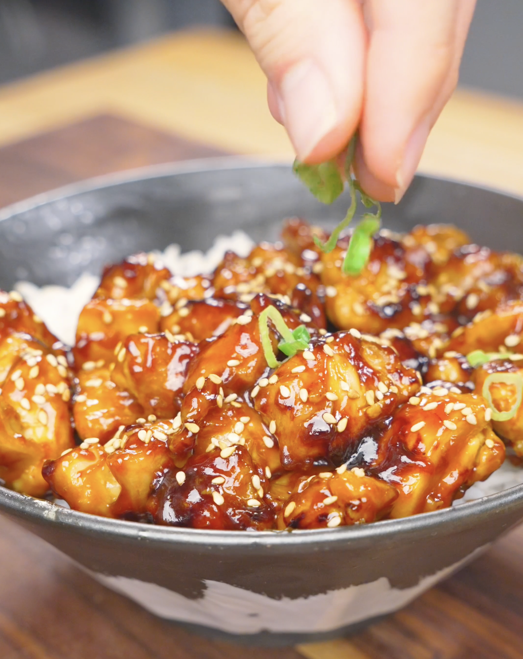 Sliced scallions being sprinkled over a caramelized, sesame-topped bowl of Honey BBQ Chicken Recipe.
