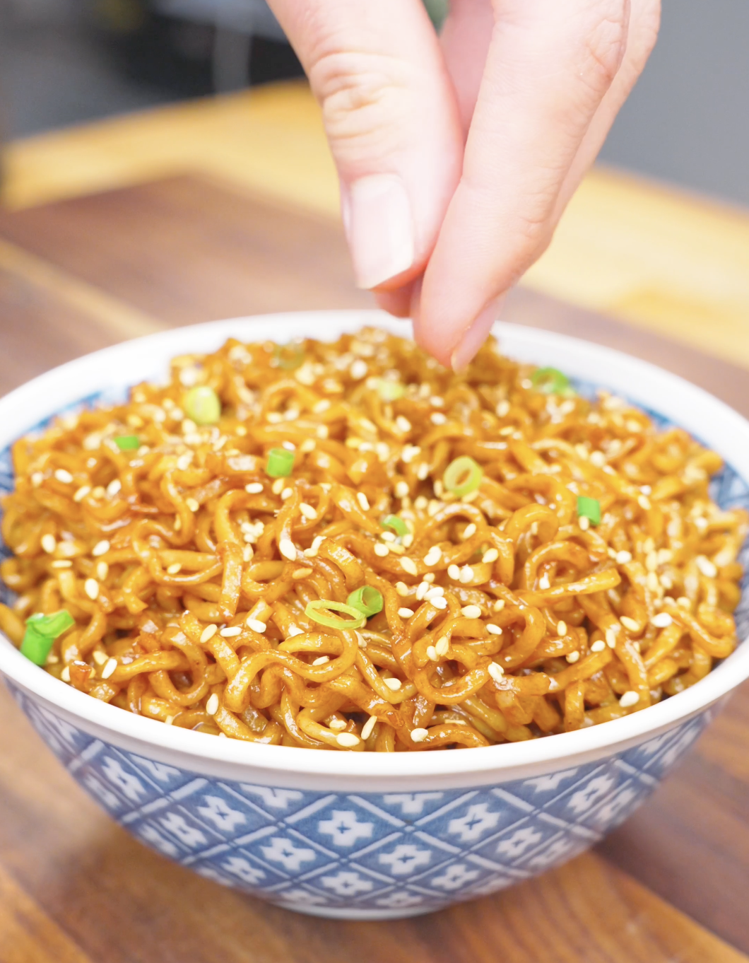 Sesame seeds being sprinkled over a scallion-topped bowl of Soy Butter Noodles Recipe.