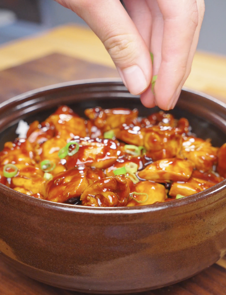 Sliced scallions being sprinkled over a clay pot of Sticky Soy Garlic Chicken Recipe.