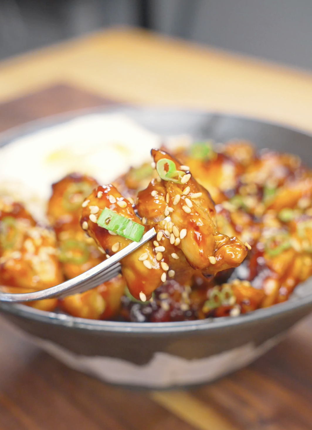 A fork lifting a sticky, sesame-coated piece above the bowl of Honey BBQ Chicken Recipe.