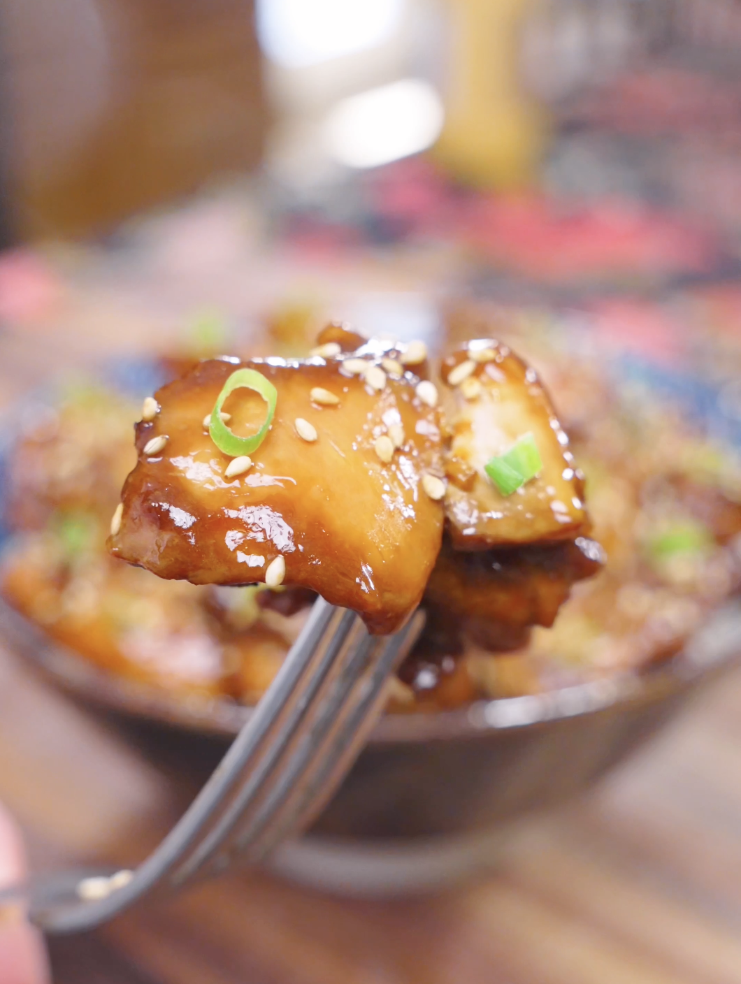 A fork lifting a glossy, sesame-topped piece above the bowl of Honey Sesame Chicken Recipe.