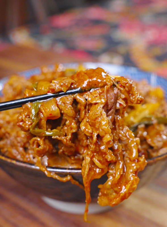 Chopsticks lifting a saucy tangle of beef and kimchi above the bowl of Kimchi Beef Stir Fry Recipe.