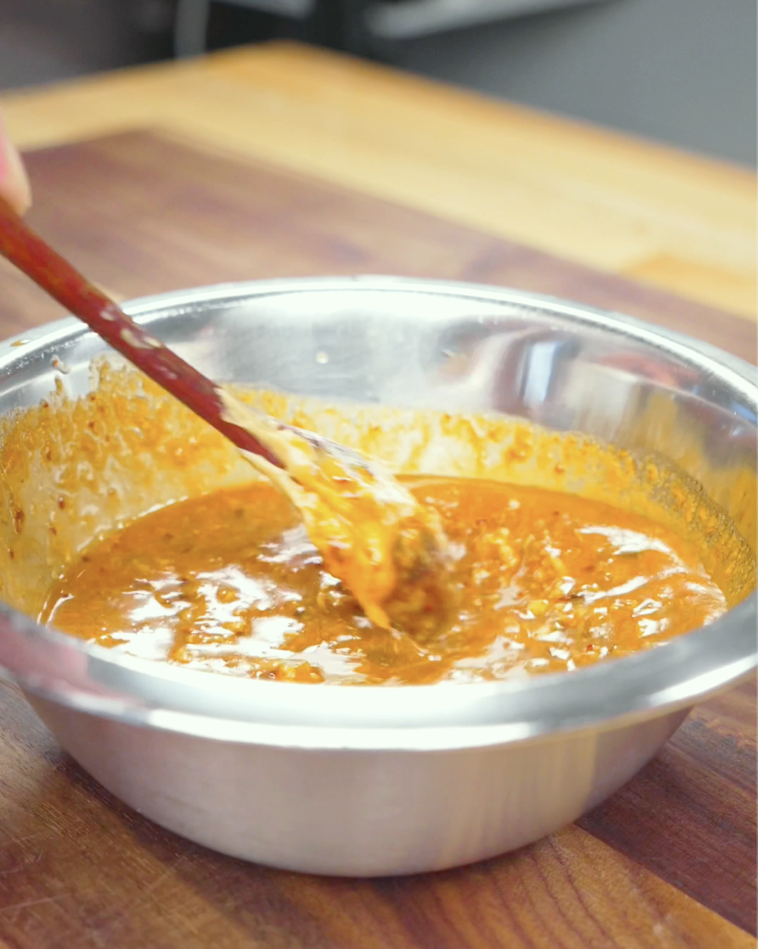 A smooth, creamy orange peanut sauce being whisked together in a metal bowl for Spicy Peanut Noodles Recipe.