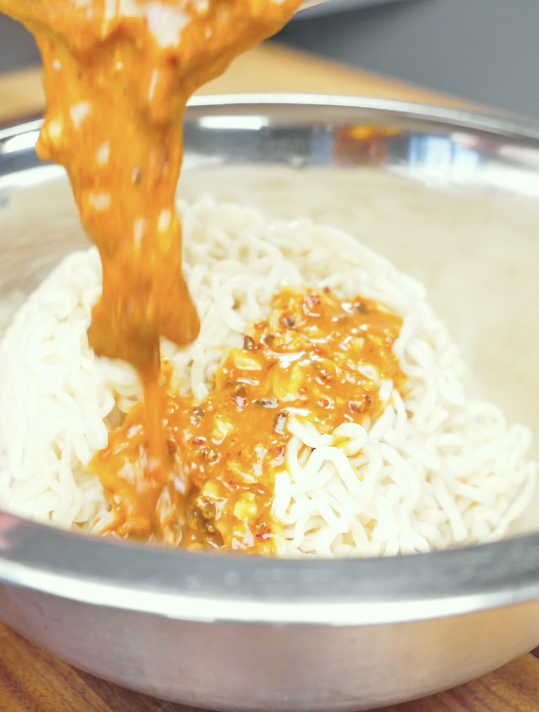 Peanut sauce being poured over cooked noodles in a mixing bowl for Spicy Peanut Noodles Recipe.