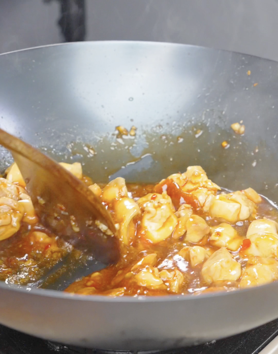 Chicken simmering in a bubbling red chili sauce in the wok for Firecracker Chicken Recipe.