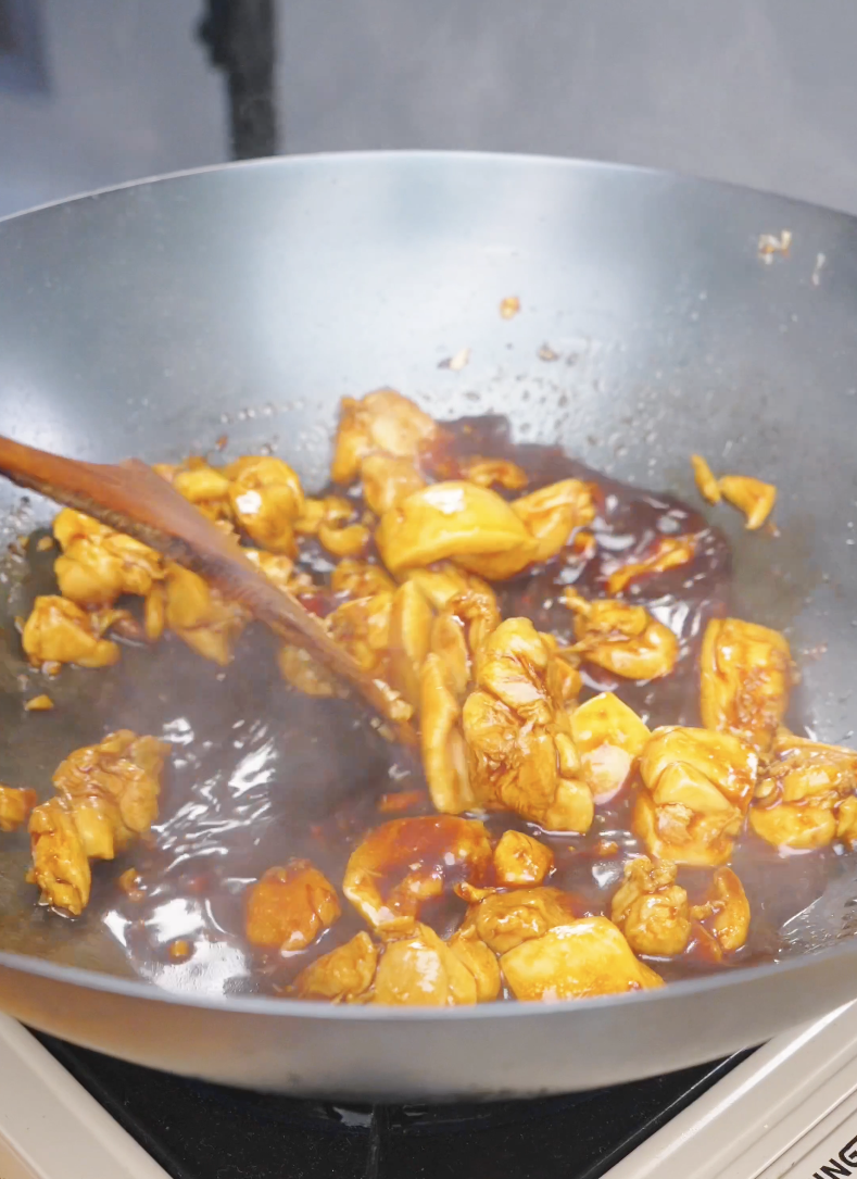 Chicken pieces simmering in a bubbling orange sauce in the wok for Sticky Orange Chicken Recipe.
