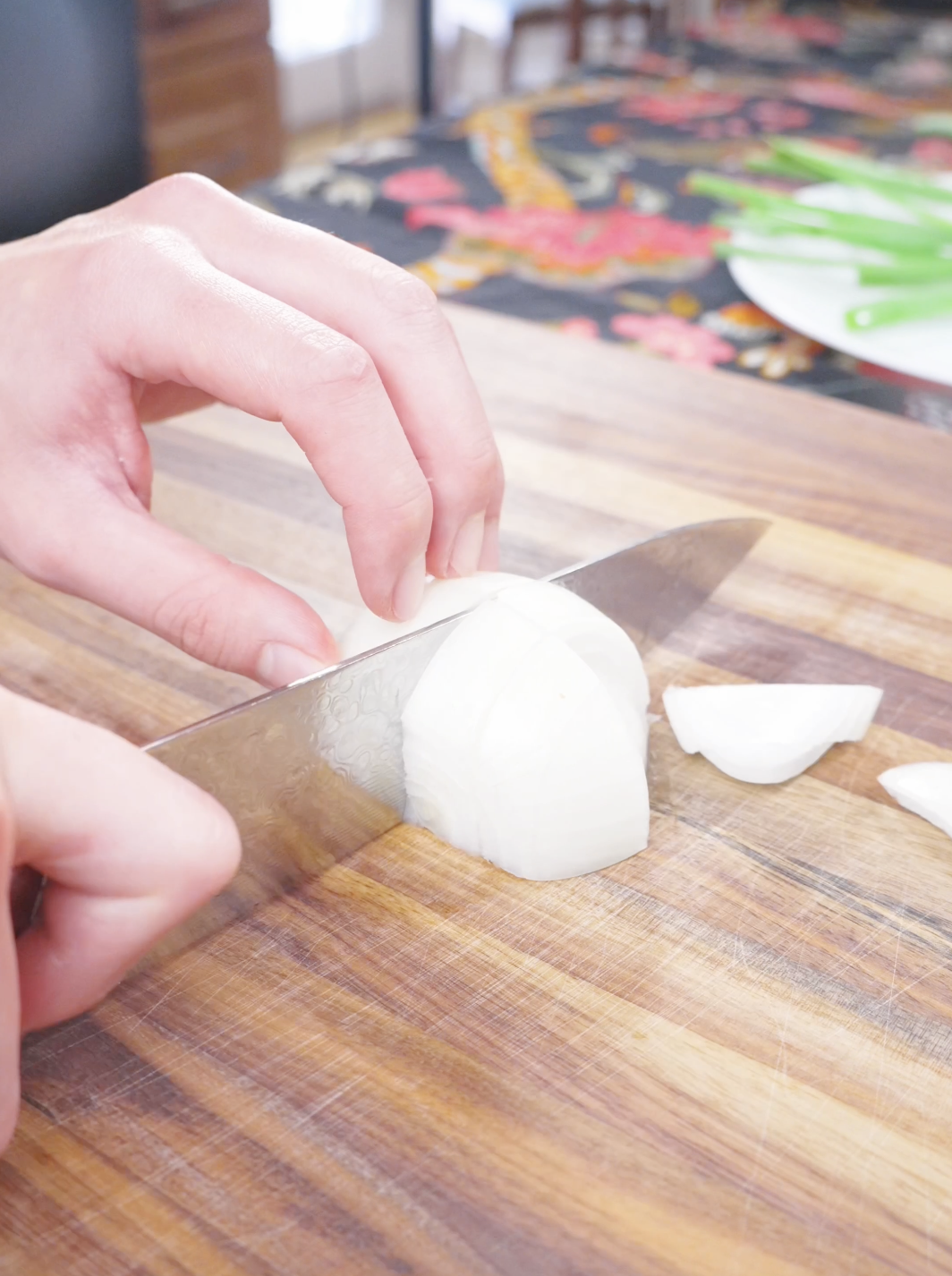 An onion being sliced with a knife on a wooden cutting board while prepping Black Pepper Chicken Udon Recipe.
