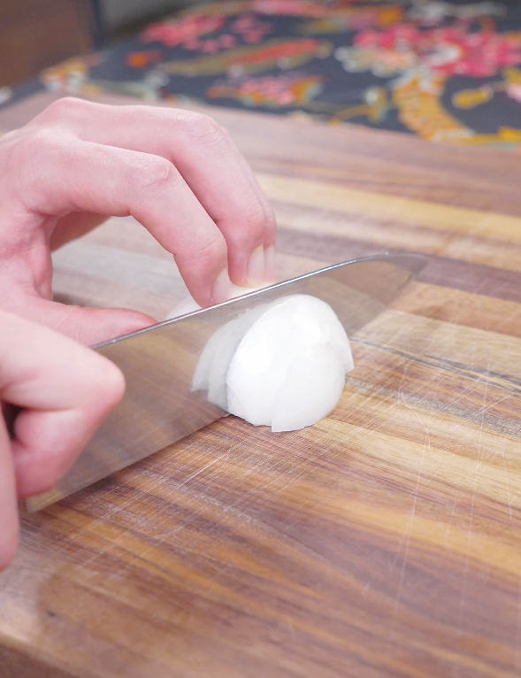 An onion being sliced on a wooden cutting board while prepping Teriyaki Beef Recipe.