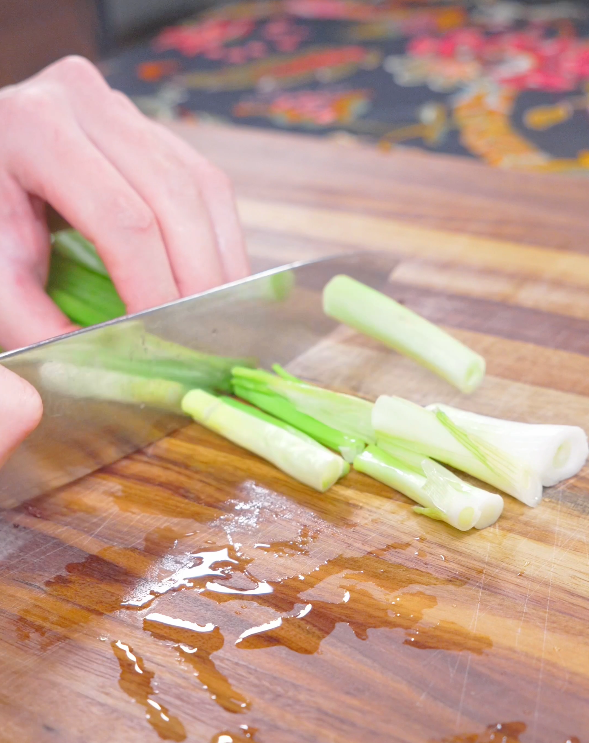 Scallions being cut into segments on a wooden board while prepping Kimchi Beef Stir Fry Recipe.