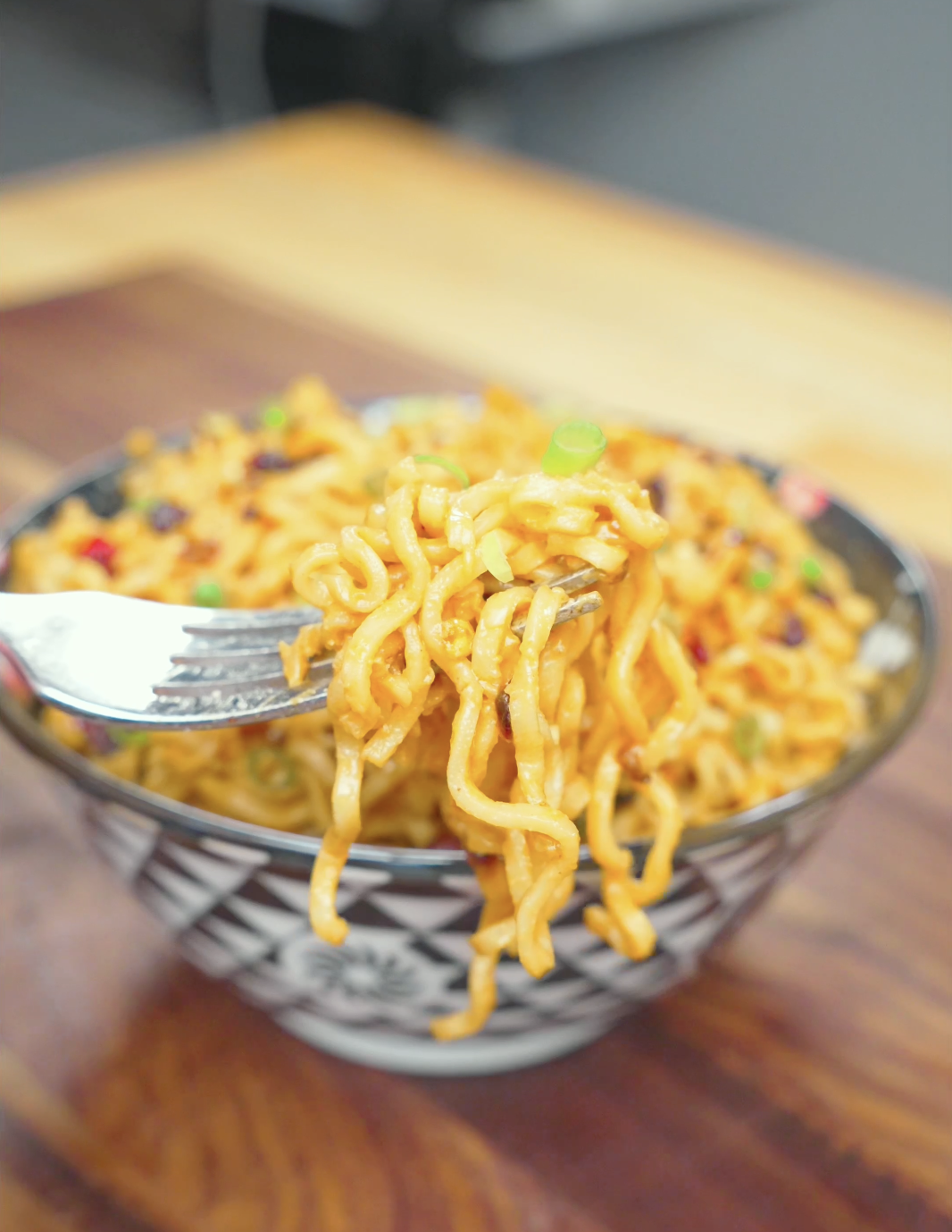 A fork lifting a twirl of creamy, sauce-coated noodles above the bowl of Spicy Peanut Noodles Recipe.
