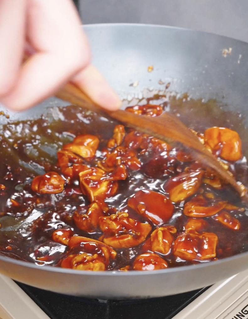 Chicken pieces being tossed in a thick, glossy orange glaze for Sticky Orange Chicken Recipe.