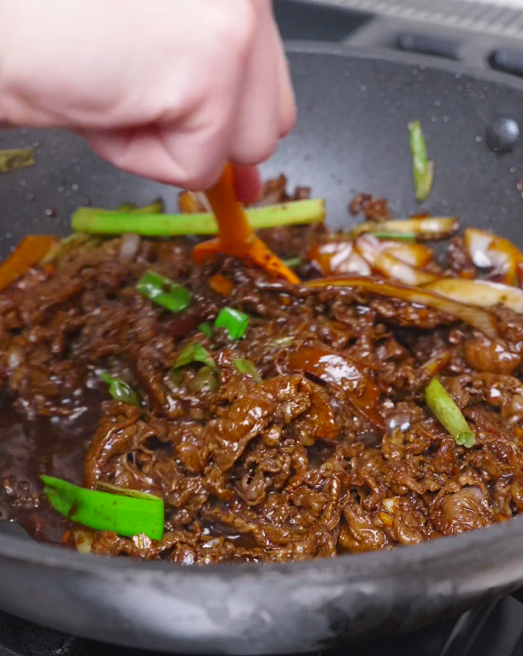 Beef and scallions being tossed in a thick, reduced glaze while finishing Teriyaki Beef Recipe.