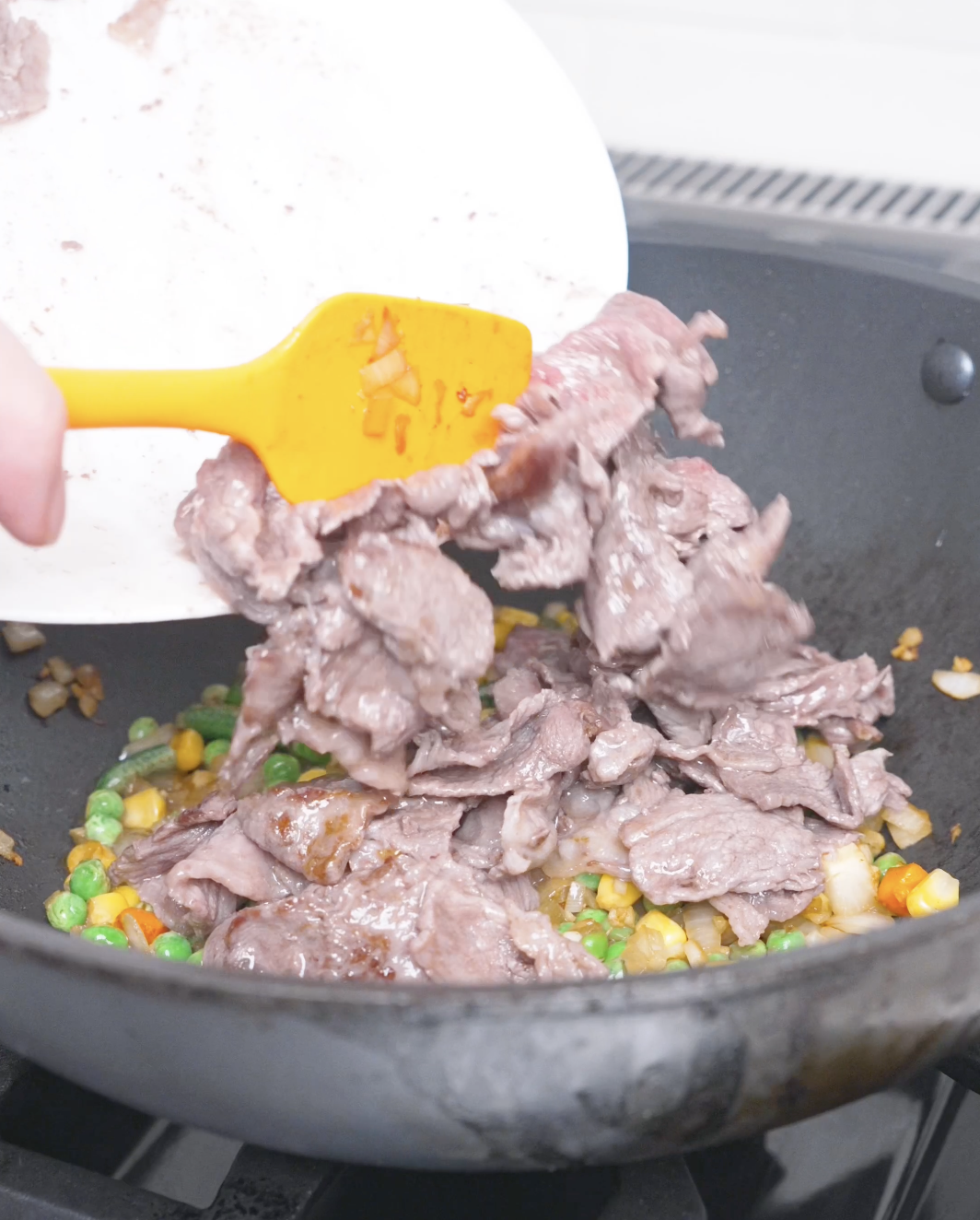 Cooked beef being returned to the wok over peas, corn, and carrots for Curry Fried Rice Recipe.