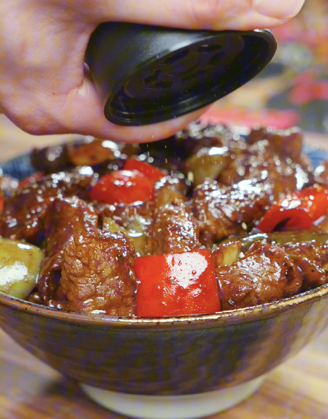 Coarsely ground black pepper being showered over a finished bowl of Black Pepper Steak Bites Recipe.