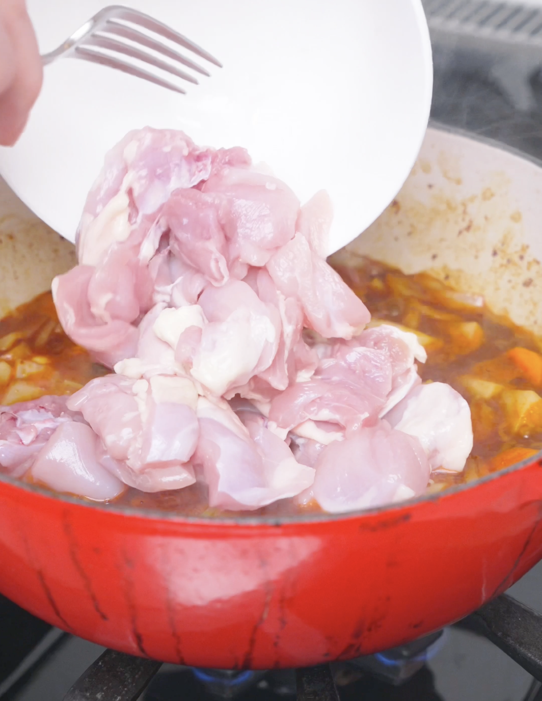 Raw chicken thigh pieces being tipped into the pot of vegetables and broth for Korean Braised Chicken Recipe.