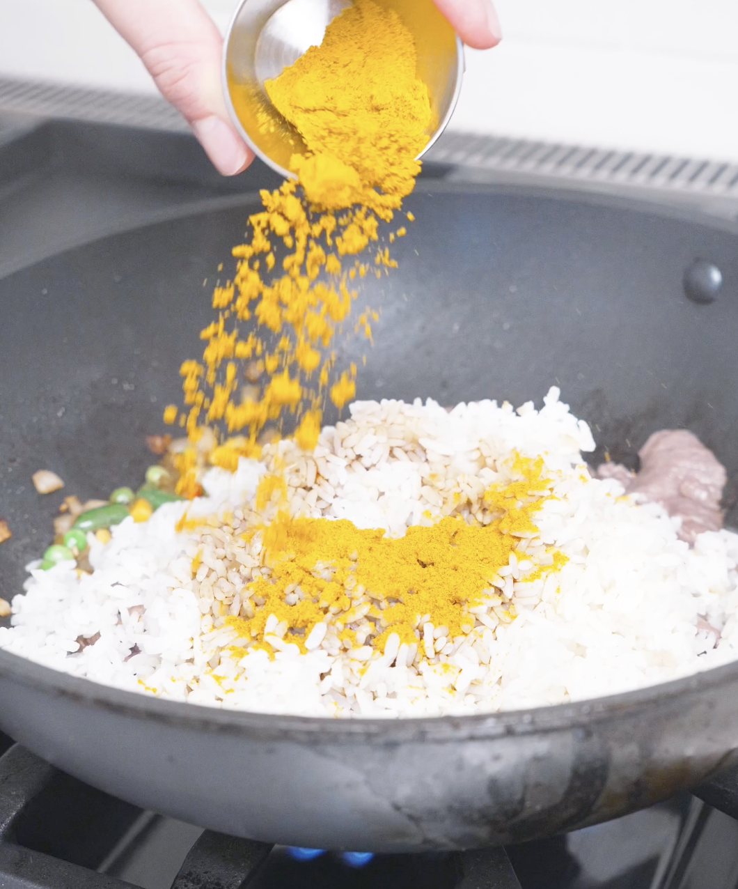 Bright yellow curry powder being poured over day-old rice in the wok for Curry Fried Rice Recipe.