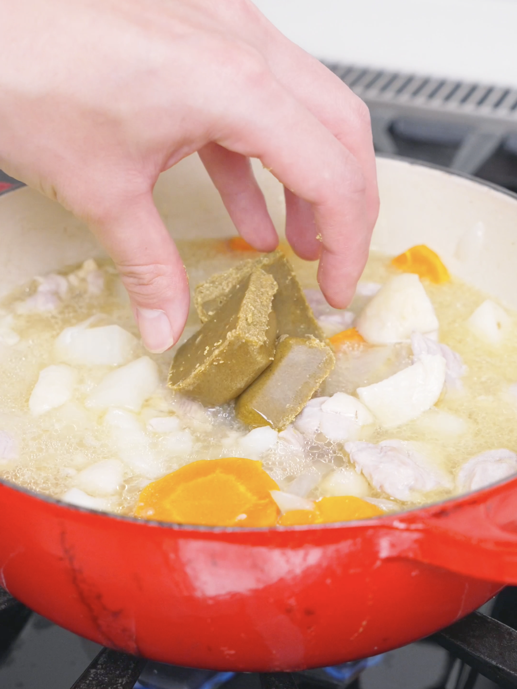Japanese curry roux cubes being lowered into the simmering pot for Chicken Curry Stew Recipe.