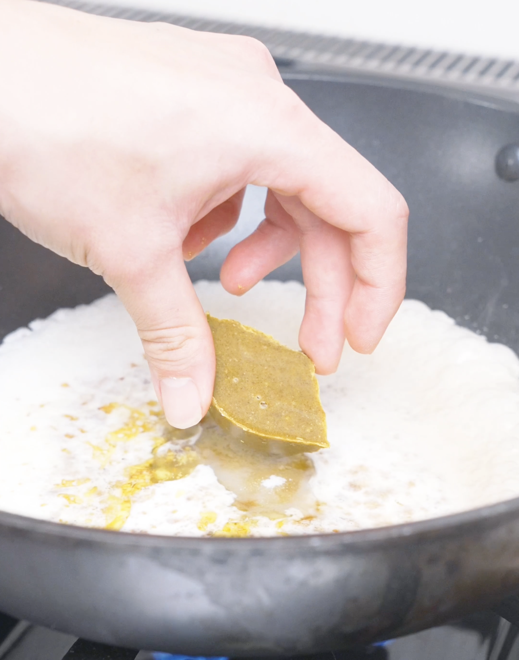A Japanese curry roux cube being dropped into simmering heavy cream for Creamy Curry Noodles Recipe.