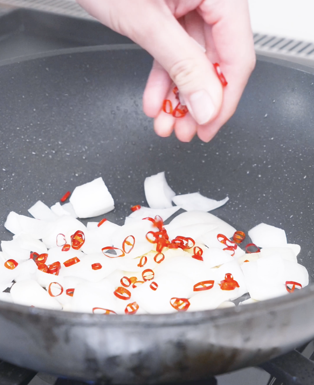 Dried red chilies being scattered over onion chunks and sliced garlic for Kung Pao Chicken Noodles Recipe.