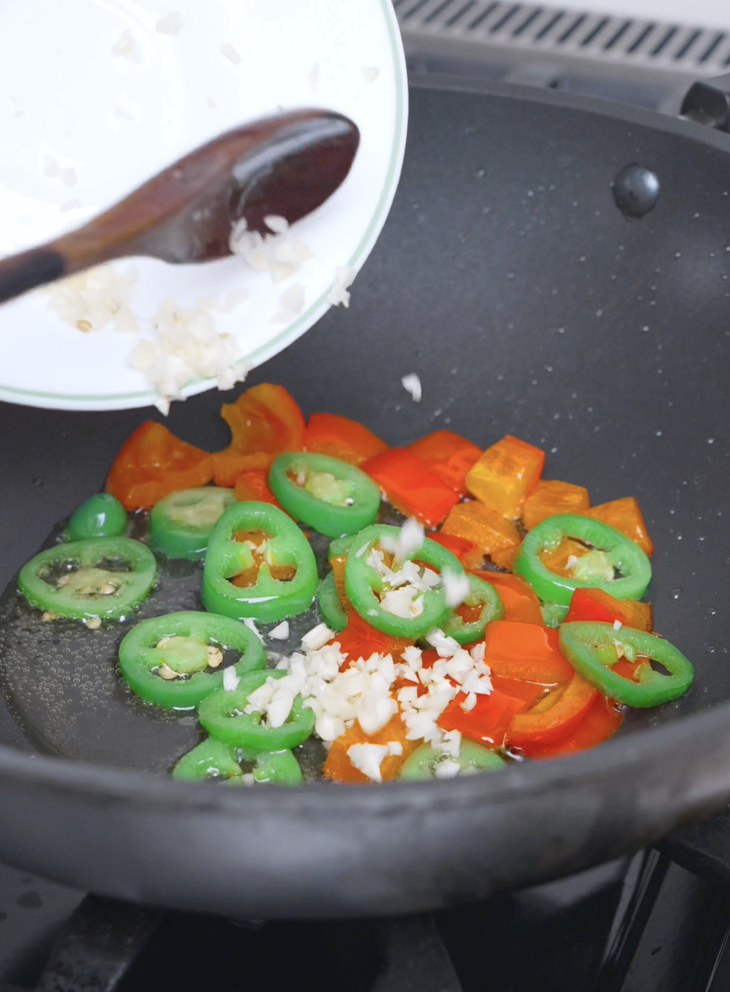 Minced garlic being tipped over the cooked peppers in the pan for Salt and Pepper Shrimp Recipe.