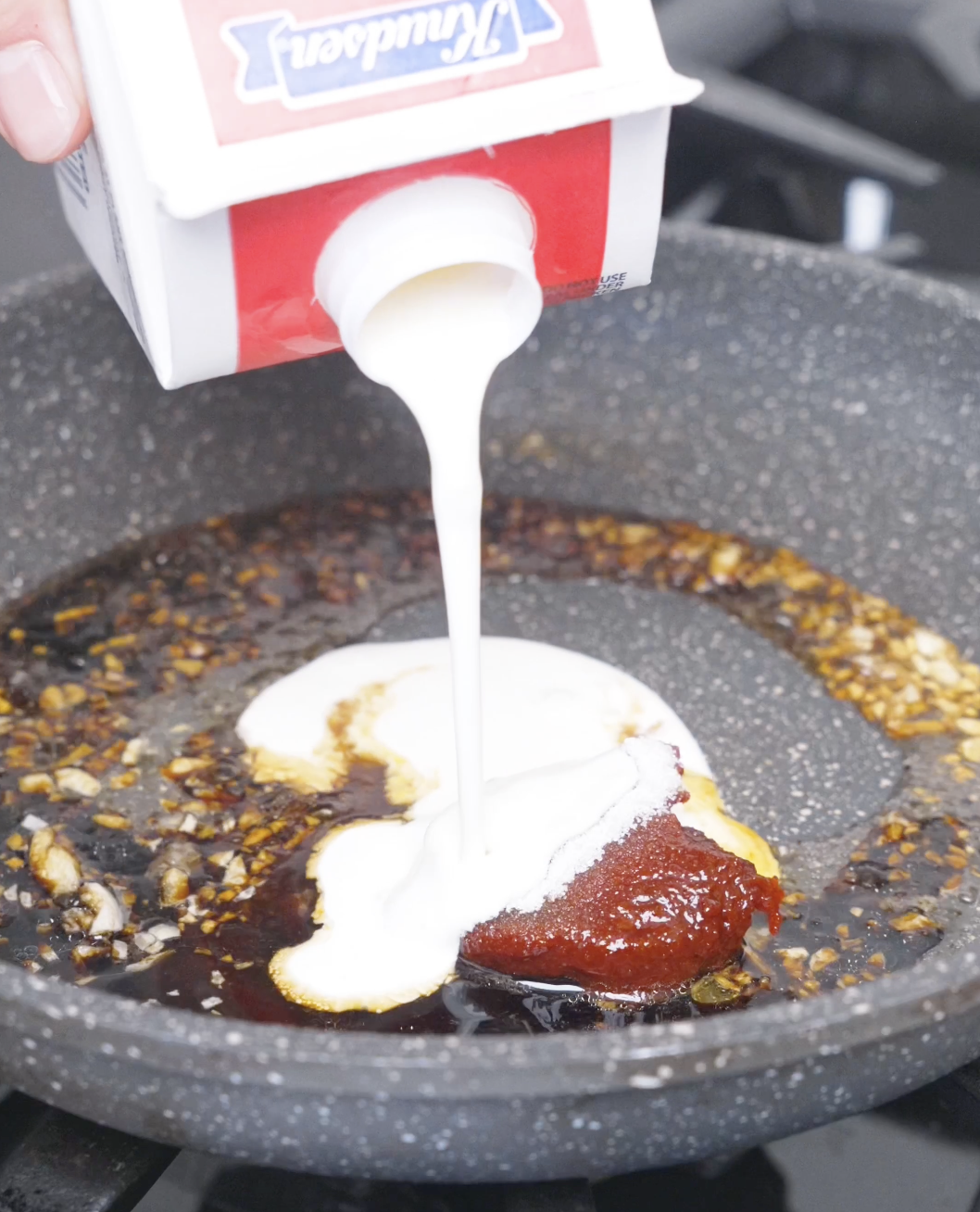 Heavy cream being poured over a spoonful of gochujang and soy sauce in the pan for Creamy Gochujang Chicken Recipe.