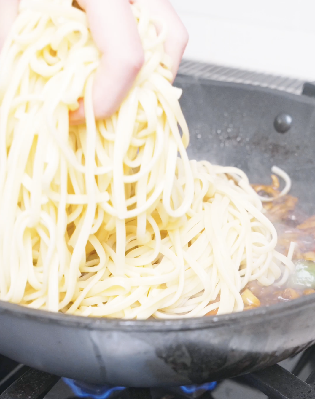Cooked noodles being dropped by hand into the wok of sauce for Kung Pao Chicken Noodles Recipe.