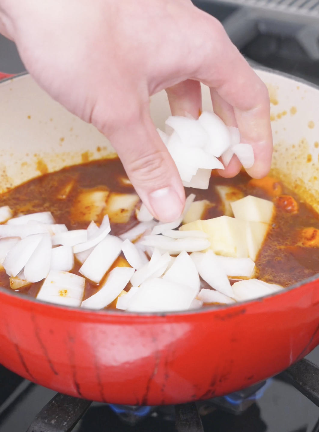 Onion chunks being dropped into the simmering broth with potatoes for Korean Braised Chicken Recipe.