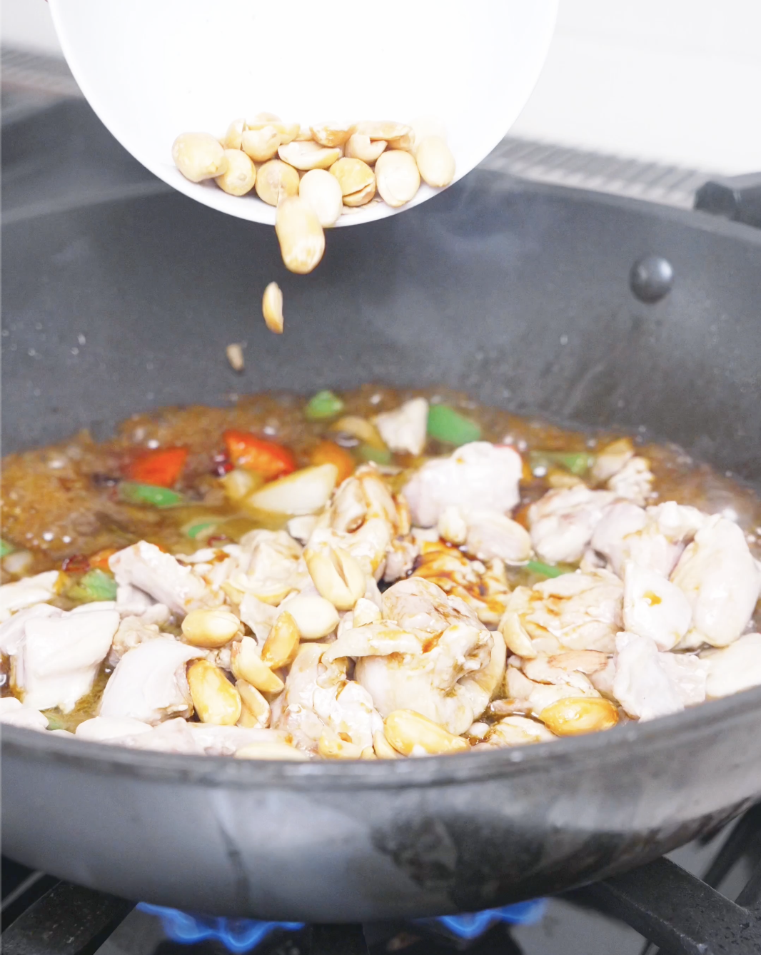 Roasted peanuts being poured into the bubbling sauce and chicken for Kung Pao Chicken Noodles Recipe.