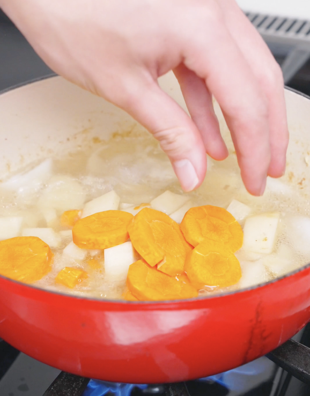 Carrot rounds being dropped in with cubed potatoes and water for Chicken Curry Stew Recipe.