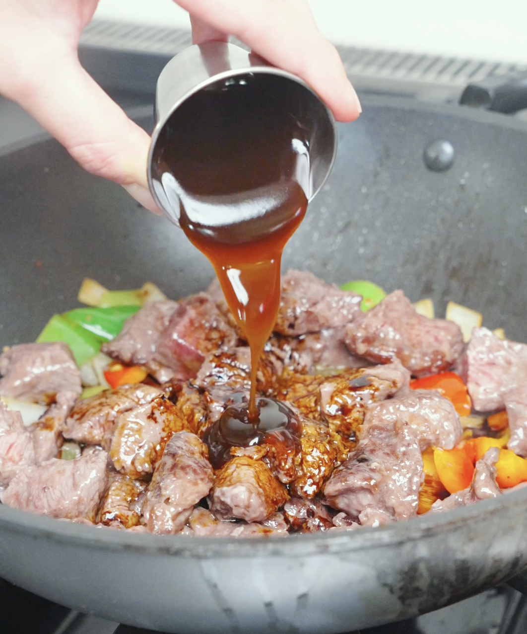 Dark soy, oyster sauce, and honey being poured over the steak and peppers for Black Pepper Steak Bites Recipe.