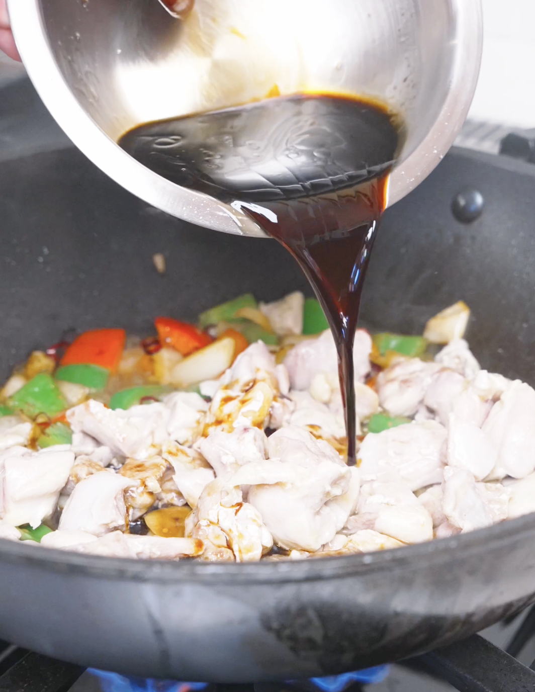 The dark hoisin and black vinegar sauce being poured over the chicken and peppers for Kung Pao Chicken Noodles Recipe.