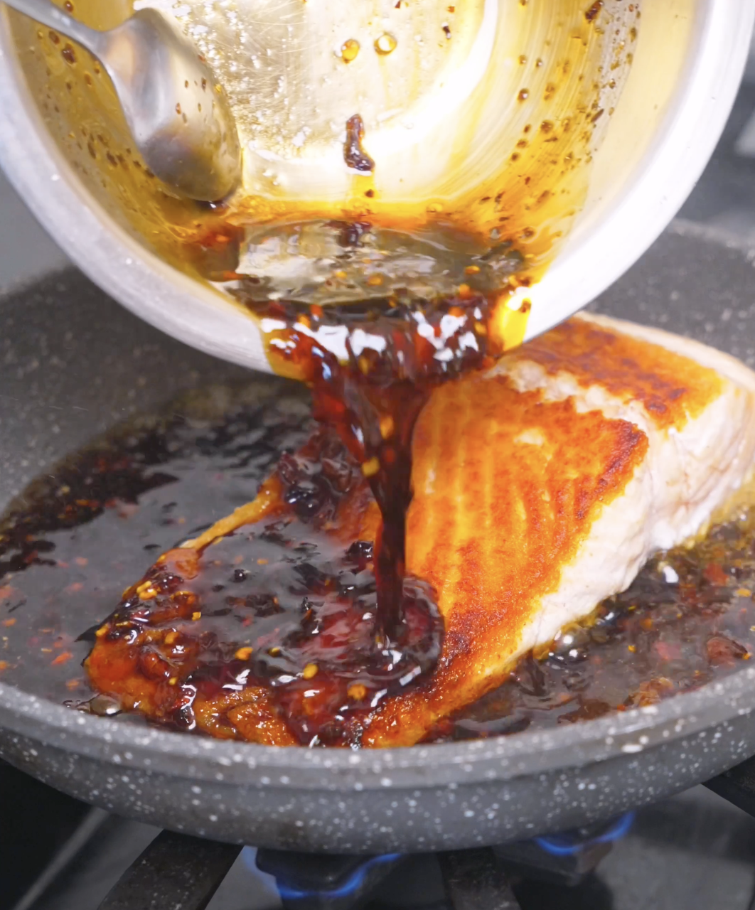 Chili crunch sauce being poured over the seared salmon in the pan for Spicy Salmon Bowl Recipe.
