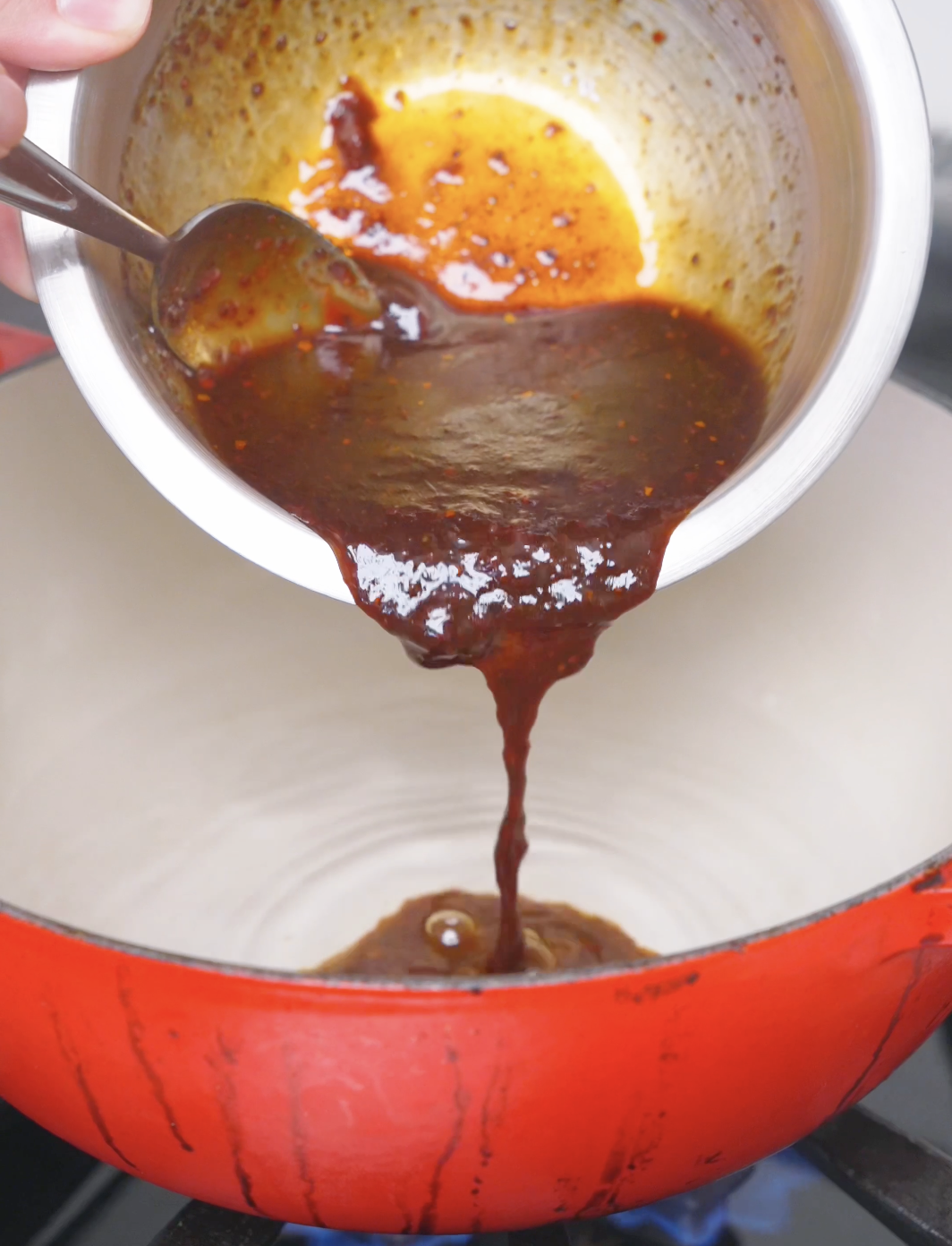 The gochujang sauce being poured into a red dutch oven to build the braising broth for Korean Braised Chicken Recipe.