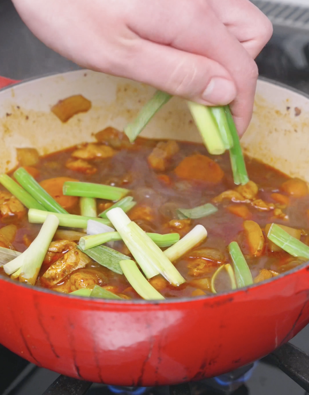 Two-inch scallion pieces being scattered over the braise for a final stir for Korean Braised Chicken Recipe.